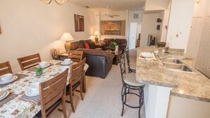 A modern living room with a sofa, dining table set, and a kitchen area with a granite countertop and bar stools. - Ip60382 - Fiesta Key - 4 Bed 3.5 Baths Townhome (Kissimmee)