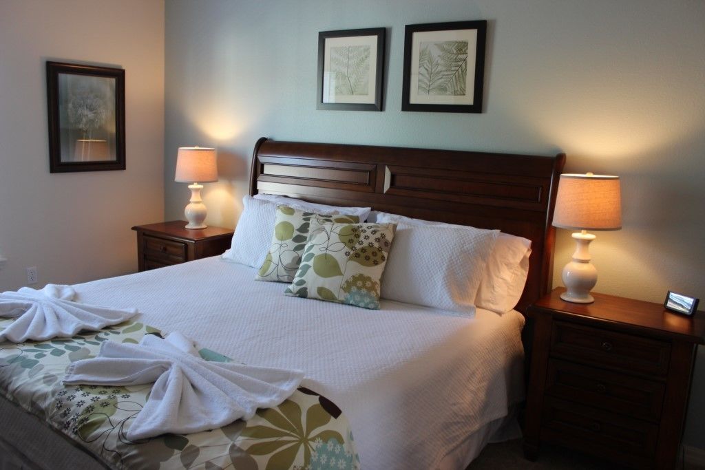 A neatly made bed with white linens and decorative pillows, flanked by two bedside tables with lamps, in a room with a simple, clean design.