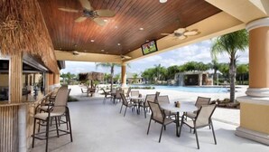 Une terrasse extérieure avec des tables et des chaises, une piscine et un écran de télévision.