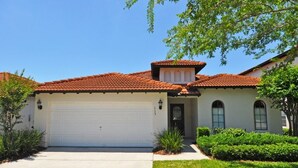 A residential house with a red-tiled roof, a white garage door, and a well-maintained front yard with shrubs and a tree.