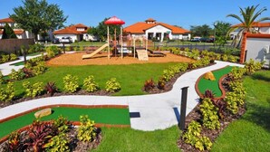 A playground with a slide and climbing structures, surrounded by landscaped garden beds and a clear sky.