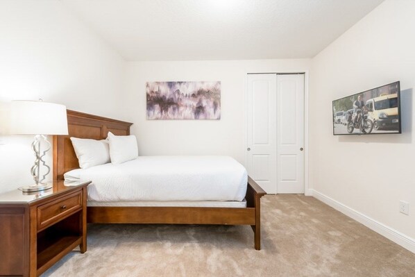 A bedroom with a wooden bed, a nightstand, a lamp, a door, and a wall-mounted painting.