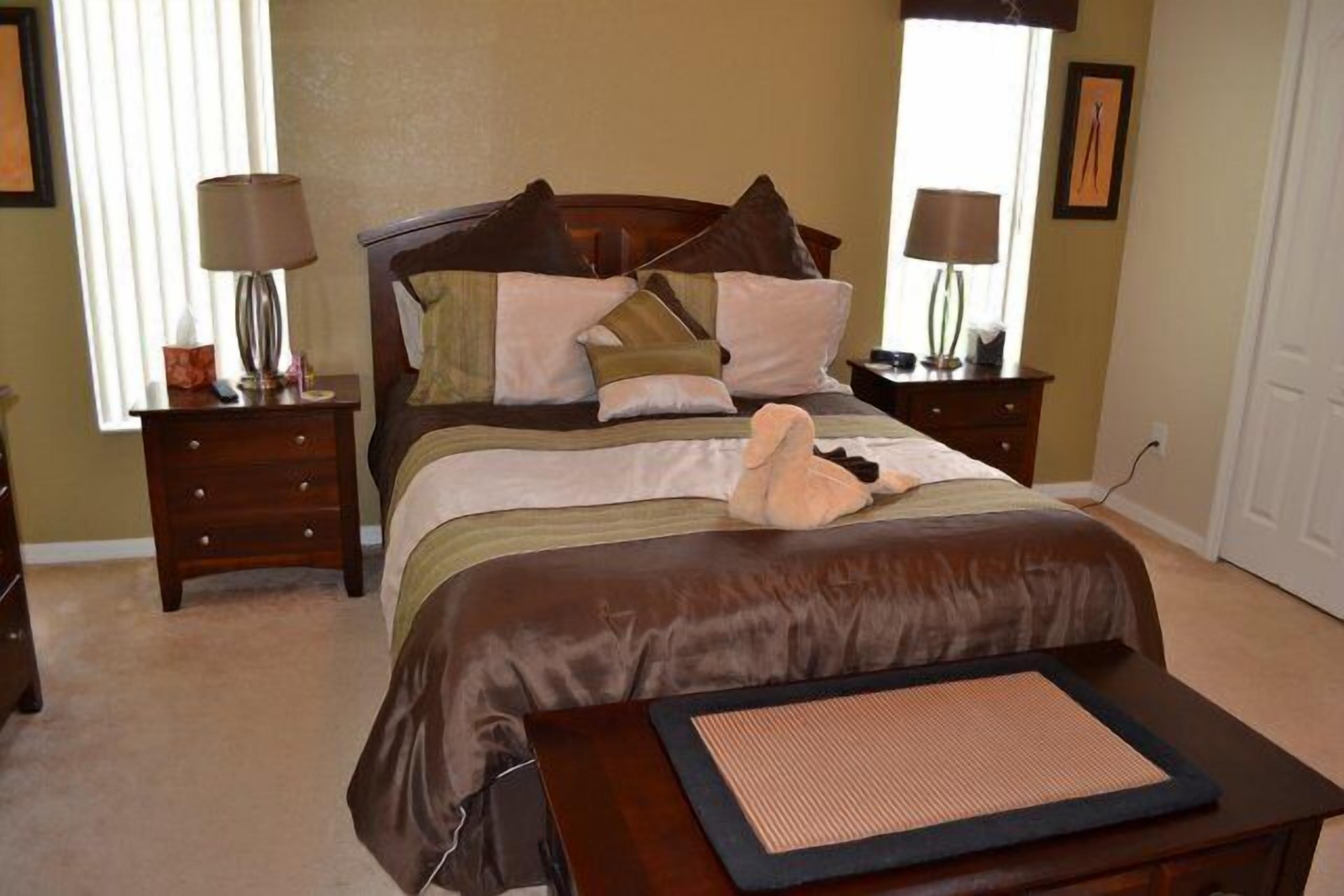 A neatly arranged bedroom with a large bed, two bedside tables, a nightstand, a lamp, and a wall-mounted picture.