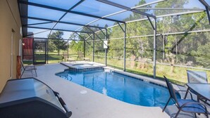 Une piscine extérieure couverte, dotée d’un jacuzzi, entourée d’une structure en verre, et un barbecue situé au premier plan.