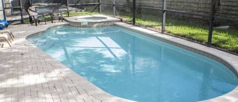 A rectangular swimming pool with a tiled deck, surrounded by a fence and a brick wall.