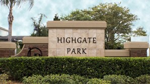 En skylt för Highgate Park med ett tydligt och lättläst typsnitt, placerad på en stenmur och omgiven av välskötta häckar och träd.