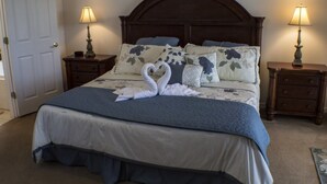 En snyggt bäddad säng med ett blått och vitt sängöverkast, två sänglampor och en dekorativ prydnadskudde formad som en svan.