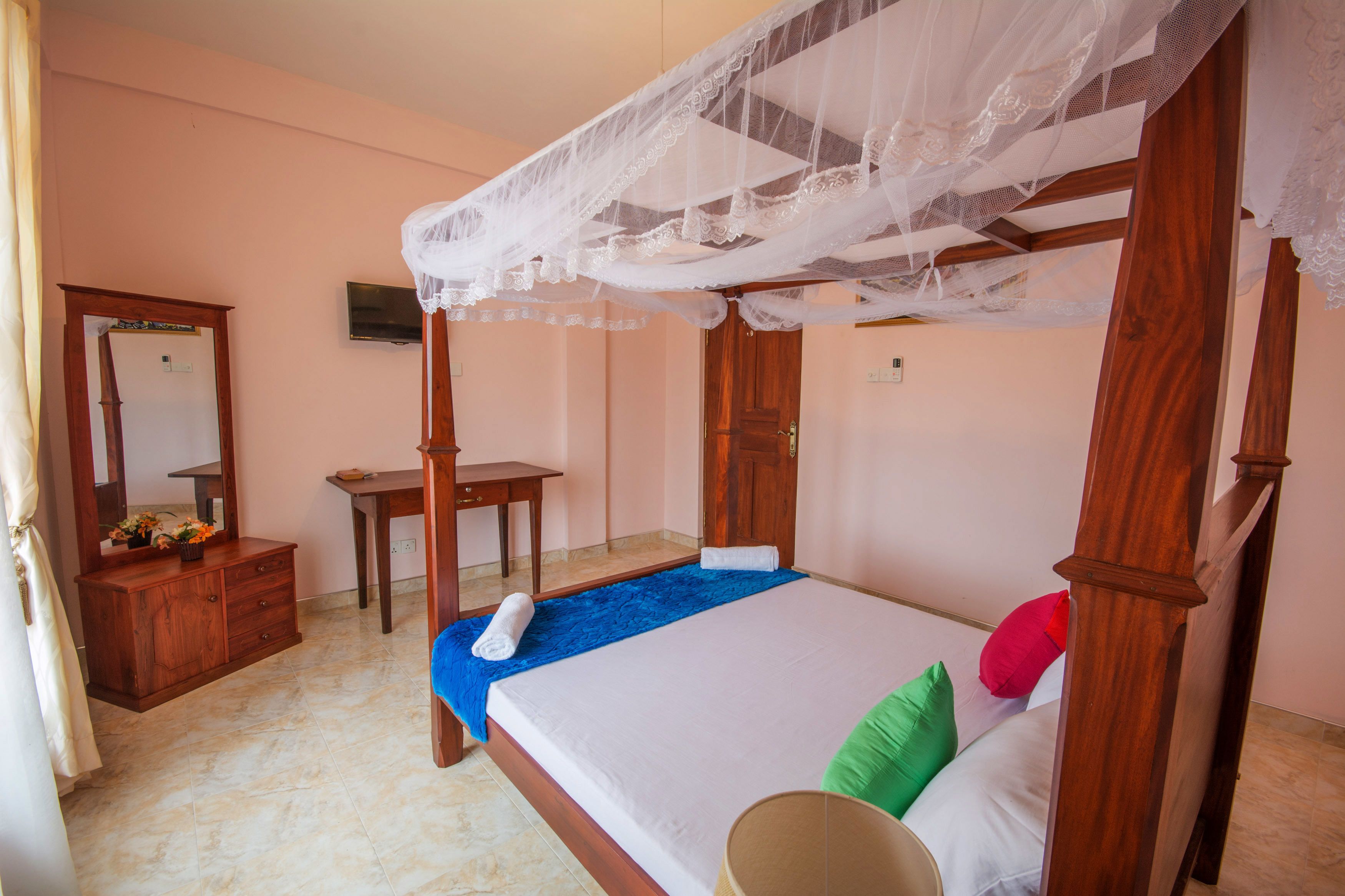 A four-poster bed with a canopy, a wooden dresser, a small table, and a mirror.