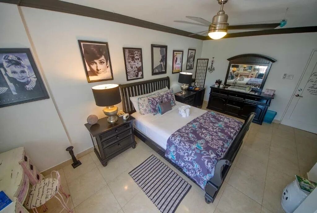 A bedroom with a bed, nightstands, a dresser, a ceiling fan, and framed pictures on the wall.