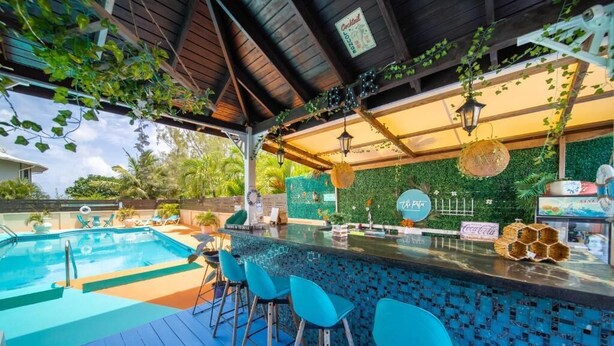 An outdoor bar area with a pool, bar stools, and a green wall with plants. - Hidden Gem Barbados (Inch Marlowe)