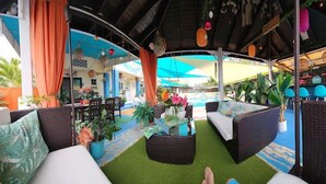 A covered outdoor seating area with wicker furniture, a small table, and potted plants.