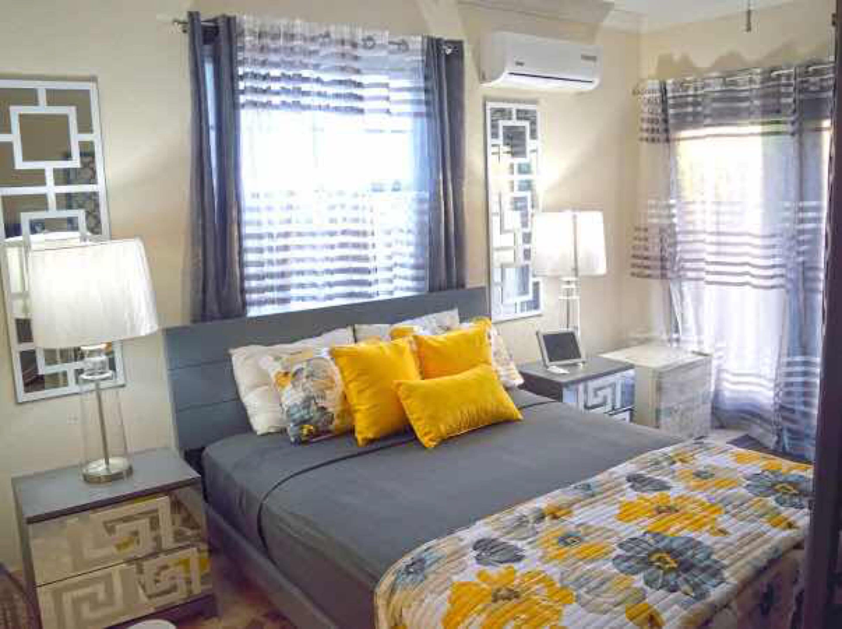 Quarto com cama, mesas de cabeceira, abajur e cortinas.
