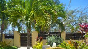 A tropical garden with palm trees, a fountain, and a building with a gated entrance. - Hidden Gem Barbados (Inch Marlowe)