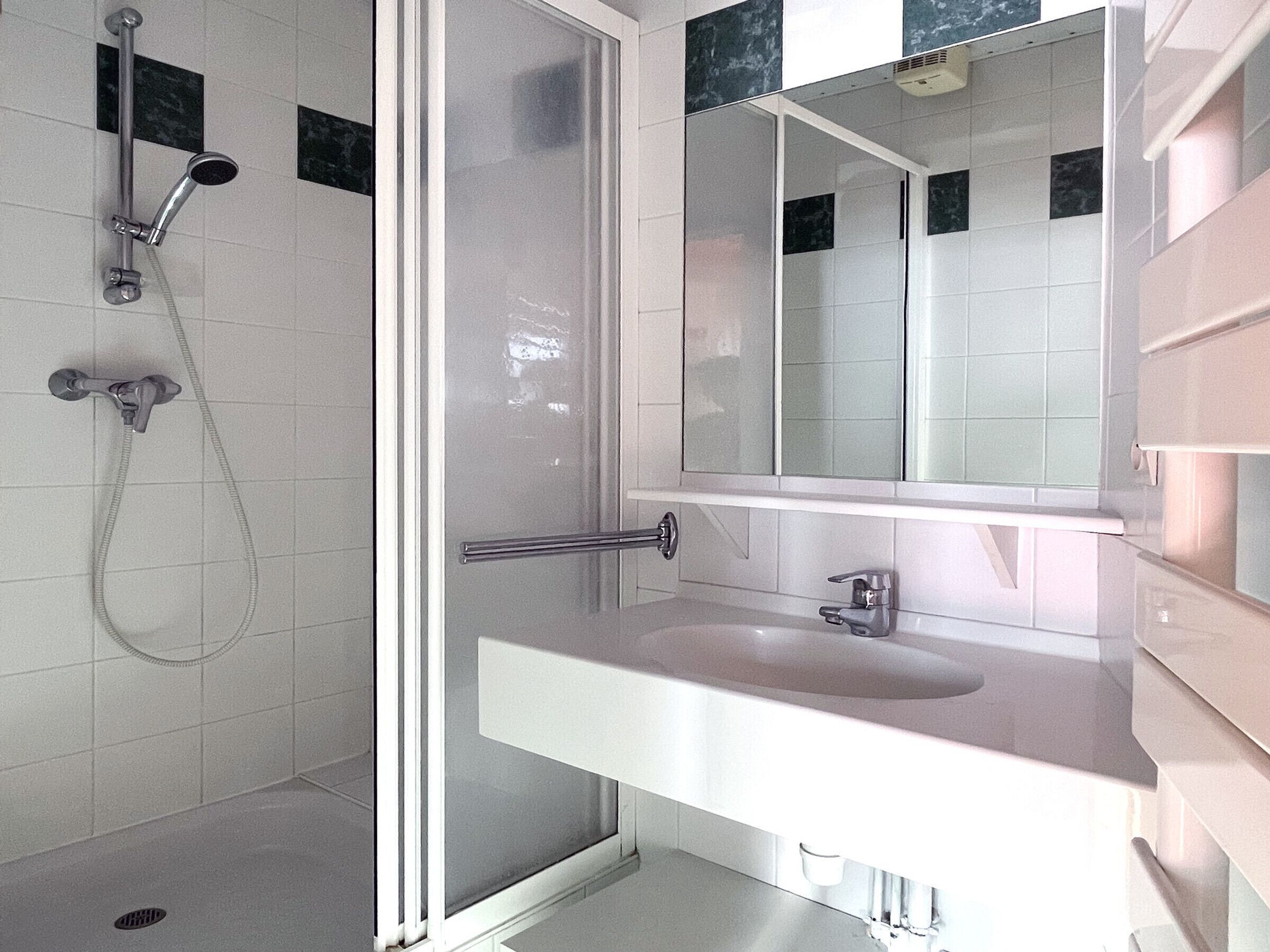 A modern bathroom with a glass-enclosed shower, a white sink, and a large mirror.