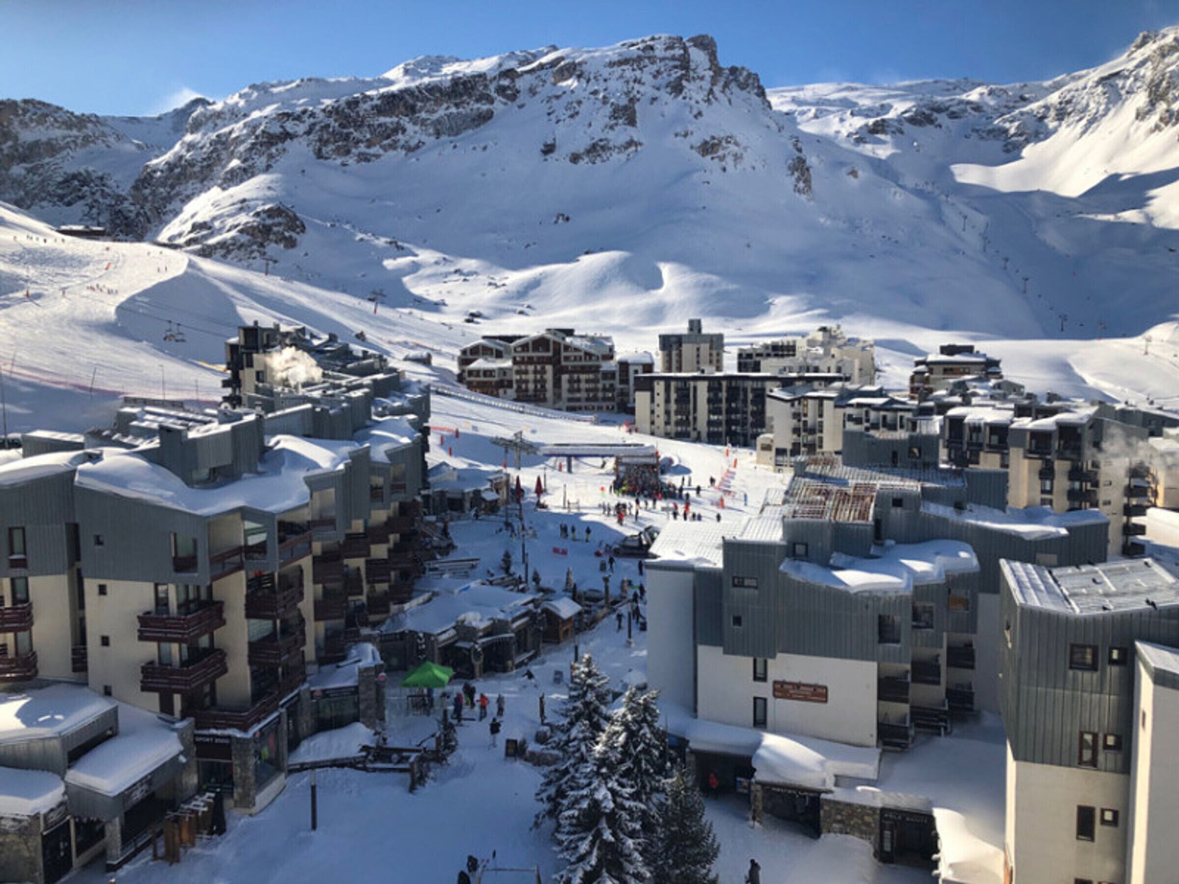 Uma cidade montanhosa coberta de neve, com edifícios, pistas de esqui e céu claro.