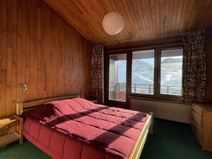 A wooden-paneled room with a bed, a window with a view of mountains, and a radiator. - 3-room ski-in/ski-out with parking, Wi-Fi included, Val Claret (Tignes)