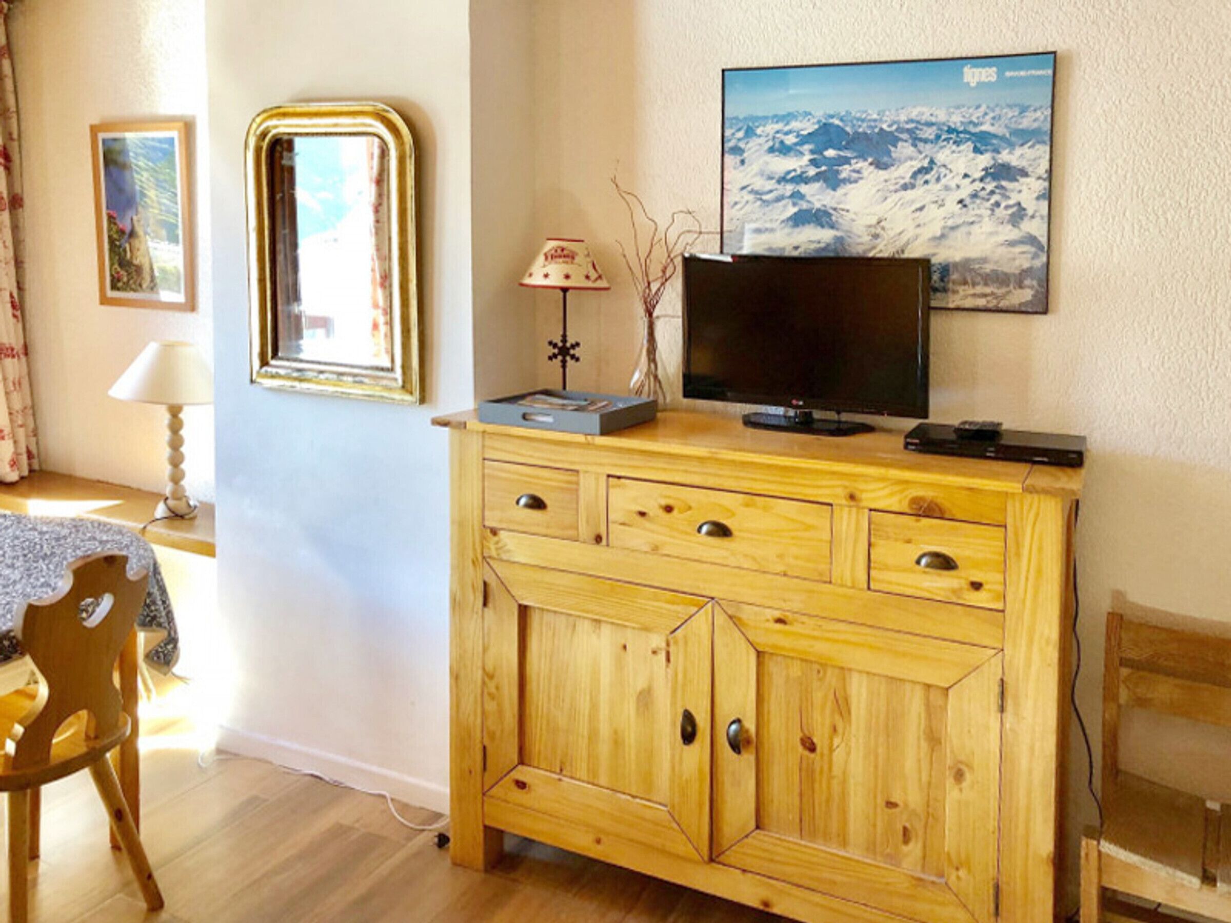 A wooden cabinet with drawers, a television on top, and a framed picture on the wall.
