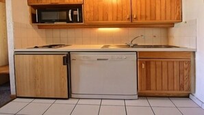 A compact kitchen with wooden cabinets, a microwave, a dishwasher, and a sink. - Cozy studio for 4 at the foot of the slopes (Plagne 1800)