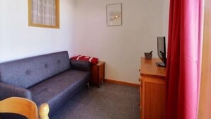 A small, sparsely furnished room with a grey sofa, a wooden cabinet, and a small table. - Cozy studio for 4 at the foot of the slopes (Plagne 1800)