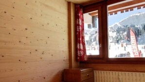 Een houten kamer met een bed, een raam met uitzicht op een wintersportgebied en een radiator.