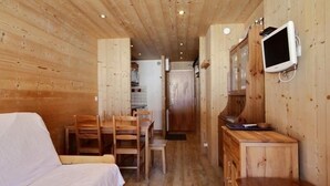 Een houten huttendeco met een bed, een eettafel, stoelen, een keukenhoekje en een aan de muur bevestigde televisie.