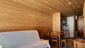 Een knus interieur van een blokhut met houten plafond, een bank, een eettafel met stoelen en een keuken.
