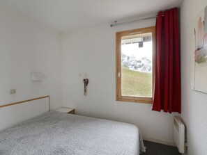 A simple room with a bed, a window with a view of mountains, a radiator, and a red curtain.