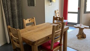 Ein Holztisch mit vier Stühlen, ein kleiner Beistelltisch, ein an der Wand befestigter Fernseher und eine Tür mit einem roten Vorhang.
