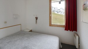 Ein schlichtes Zimmer mit einem Bett, einem Fenster mit Bergblick, einer Heizung und einem roten Vorhang.