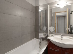 A modern bathroom with a bathtub, two sinks, and a glass shower enclosure.