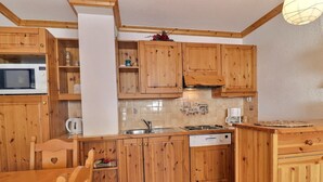 A kitchen with wooden cabinets, a microwave, a sink, and a stove. - Cozy 4 Pax with Sunny Balcony (Méribel)