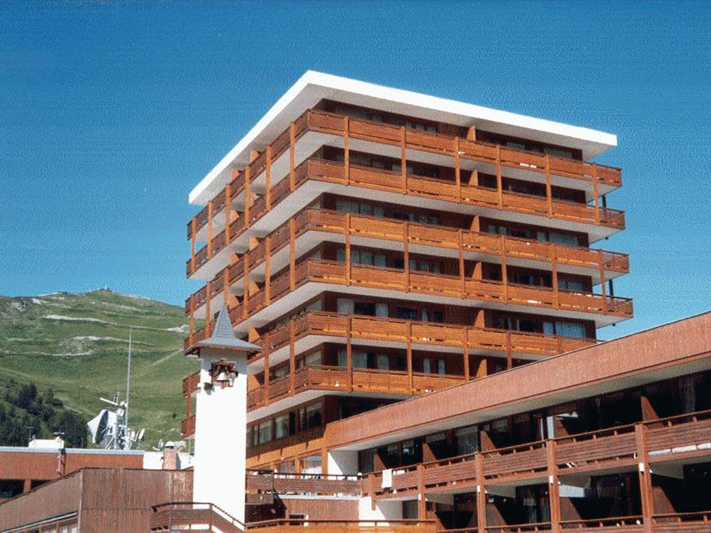 Ein mehrstöckiges Hotel mit Balkonen und einem Skilaufhang im Hintergrund.
