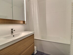 A bathroom with a white sink, wooden vanity, and a mirror.