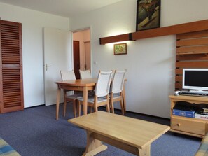 Una habitación compacta con una mesa de comedor de madera y sillas, un televisor pequeño sobre un mueble de madera, y una puerta que da a otra habitación.