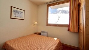 A hotel room with a bed, a window with curtains, a wall-mounted lamp, and a framed picture.