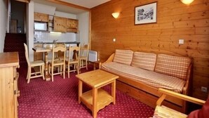 A compact living space with a wooden interior, a kitchenette, a dining area, and a sofa.