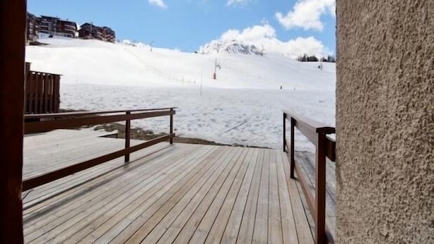 A wooden deck leading to a snowy landscape with a mountain in the background.