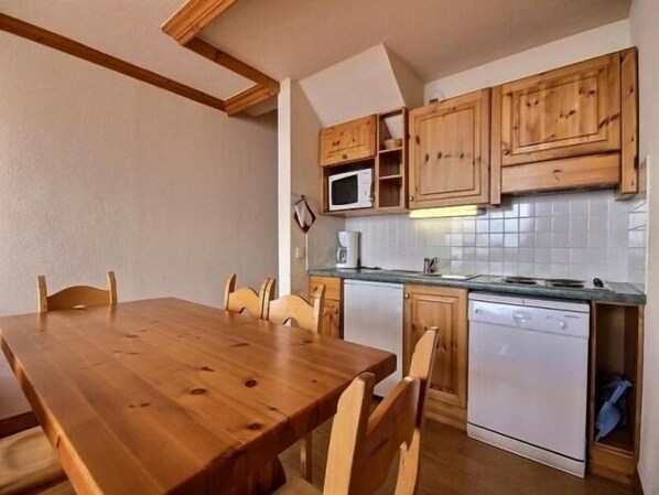 A compact kitchen with wooden cabinets, a microwave, a dishwasher, and a dining table with chairs.