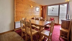 A wooden-paneled room with a large table and chairs, a window with a view of the beach, and a small desk with a lamp.