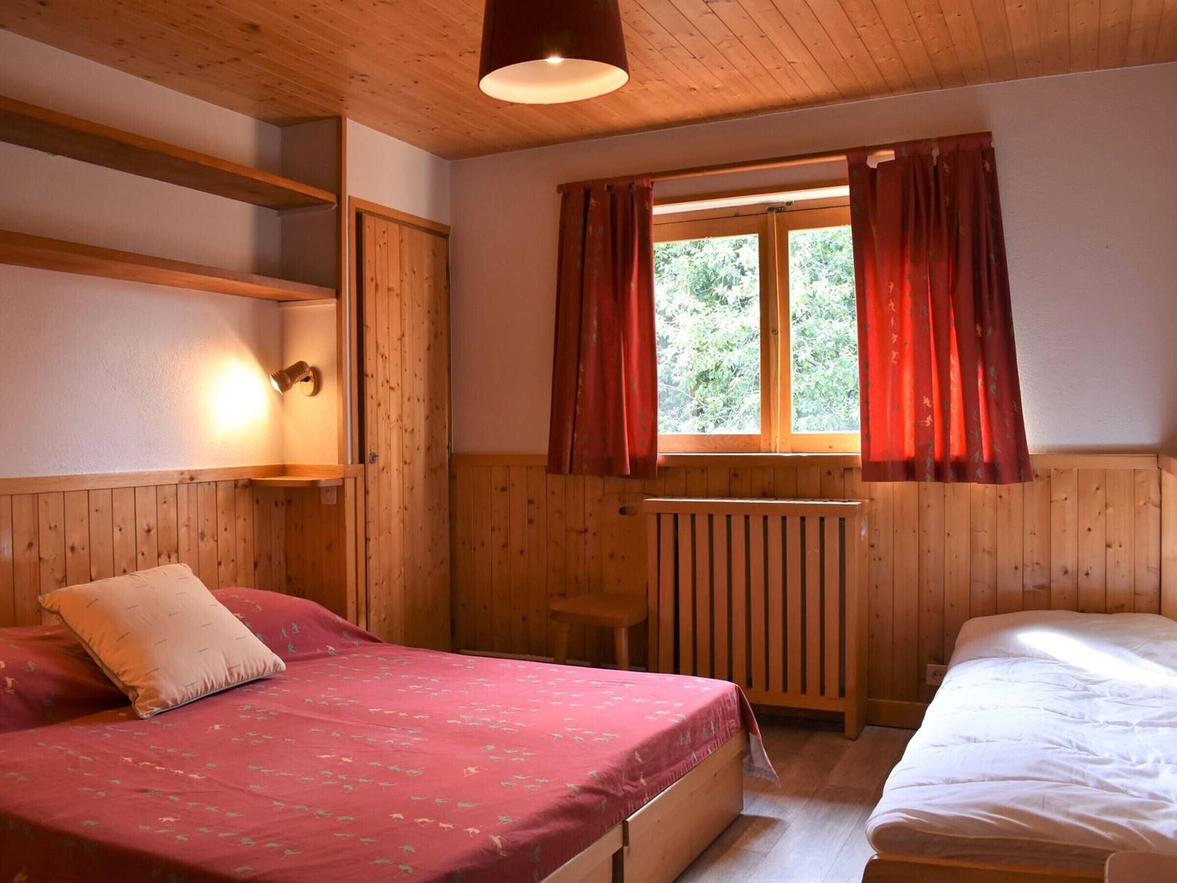 Una habitación de madera con cama, una mesita y una ventana con cortinas.