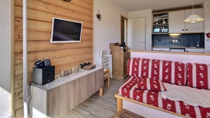 A cozy living area with a wooden wall, a flat-screen TV, a clock, a sofa, and a kitchen area with cabinets and a microwave. - Apartment 6 people, south-west terrace at slopes' foot (Belle Plagne)