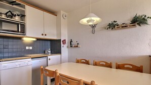 A compact kitchen with white cabinets, a microwave, a sink, and a dining table with wooden chairs. - Apartment 6 people, south-west terrace at slopes' foot (Belle Plagne)