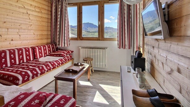 A cozy room with a wooden interior, a sofa with patterned cushions, a small table, a television mounted on the wall, and a window offering a view of the outdoors. - Apartment 6 people, south-west terrace at slopes' foot (Belle Plagne)