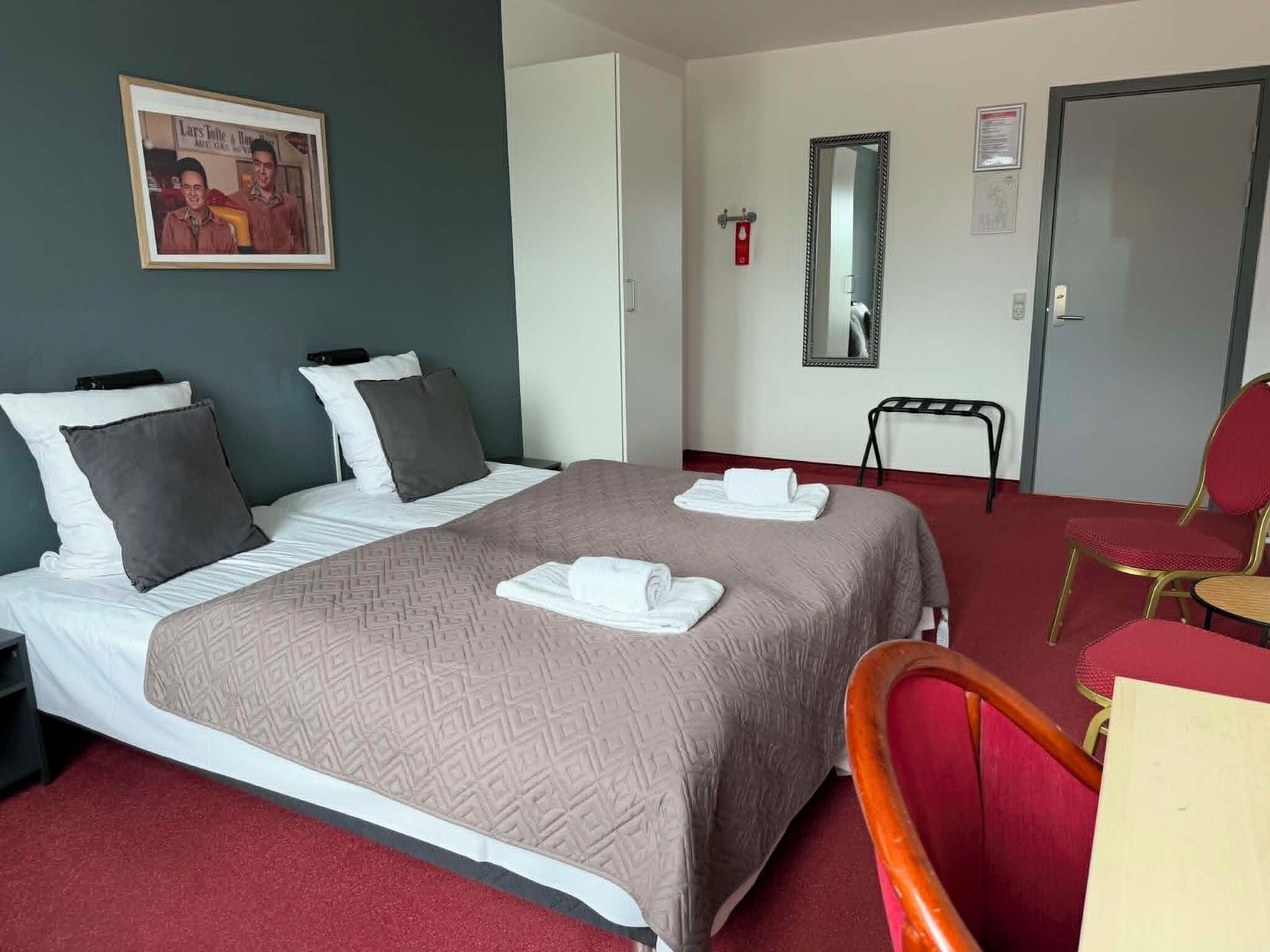 Et hotelværelse med en seng, to puder, et natbord, en stol, et spejl og en dør.
