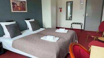 Et hotelværelse med en seng, to puder, et natbord, en stol, et spejl og en dør.