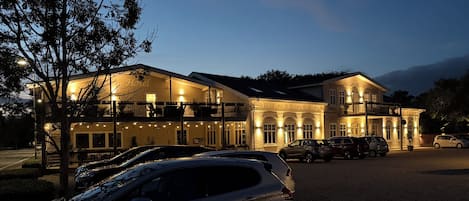 A hotel with a two-story structure, multiple balconies, and a parking area with several cars.