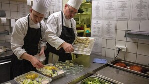 Chefs preparing food in a kitchen with stainless steel counters and various food items. - Hotel Kløver Es (Rodekro)