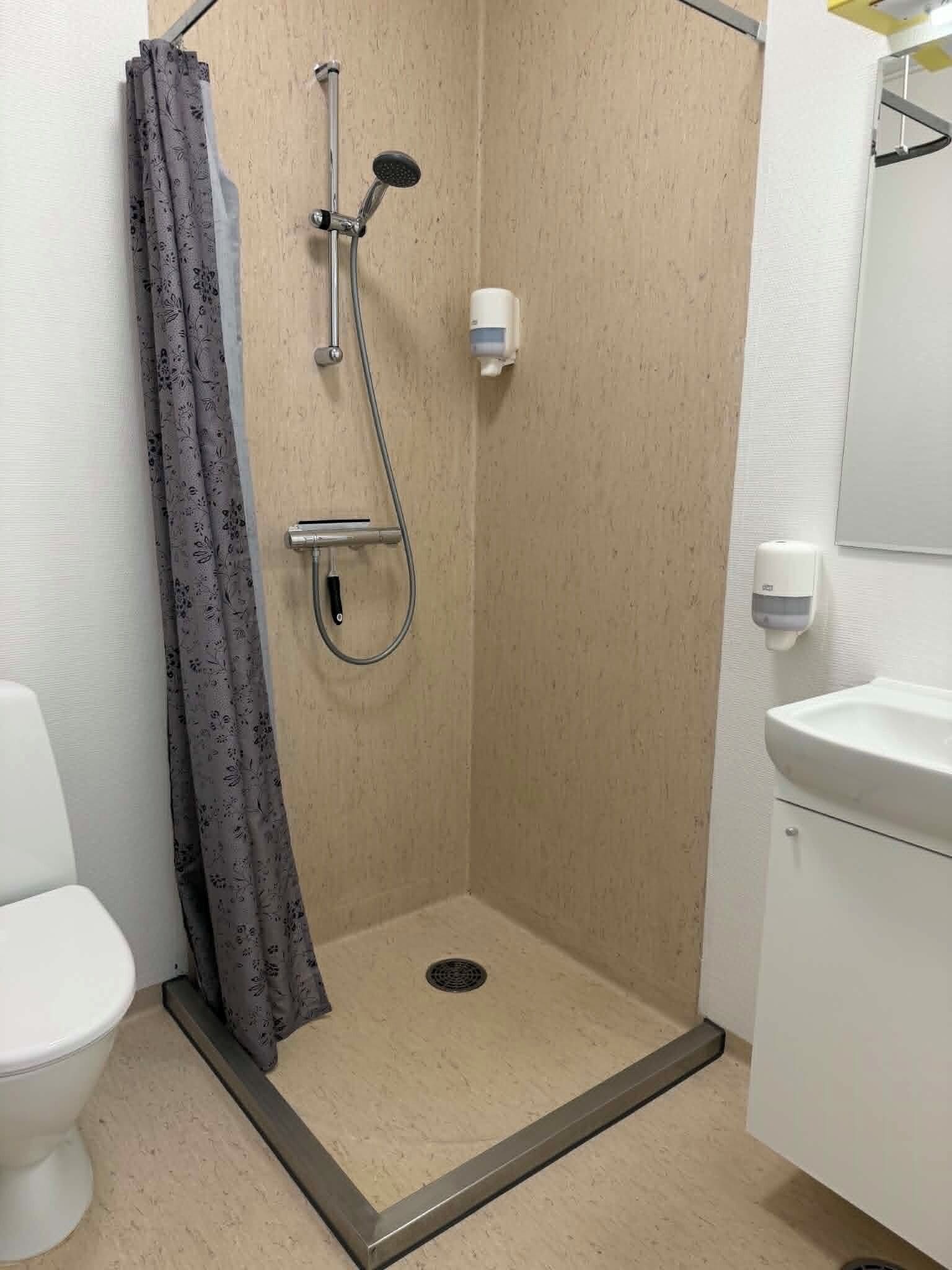 Et lille, lukket bruseområde med brusehoved, håndbruser og toilet.