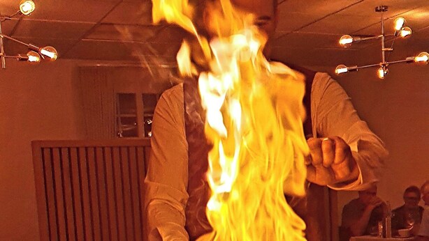 A person performing a fire act with flames rising from a pot on a table. - Hotel Kløver Es (Rodekro)