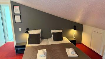 Una habitación de hotel con una cama, dos mesitas de noche, una lámpara de pared y una puerta.